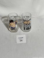 Two clear glass tumblers with WWF logo and wrestler graphics side-by-side on white cloth.