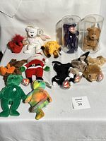 Full lot of 12 Beanie Babies shown on table. Includes various colors and characters including red devil, white bear, yellow dog, two bears in cases, and a moose.