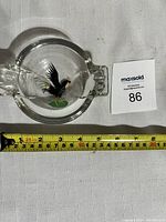 Clear glass ashtray with painted black rooster in center and two rectangular cigarette rests, shown with measuring tape for size.