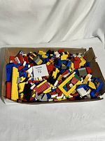 Cardboard box filled with assorted vintage LEGO bricks of various colors and sizes viewed from above.