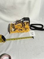Side view of the yellow diecast metal John Deere bulldozer crawler tractor with one black rubber track off to side, measuring tape placed for scale showing approx. 10 inches length.