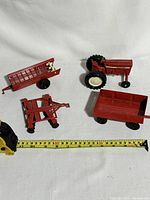Group photo of 4 Ertl farm equipment diecast pieces including tractor and accessories with measuring tape showing size