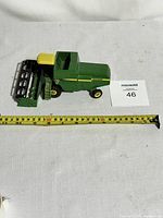 Side view of green and yellow metal John Deere farm equipment toy with yellow seat, measuring tape showing approximately 12 inches in length.
