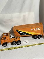 Side view of the large orange steel Tonka tractor and Allied Van Lines box trailer with measuring tape for scale.