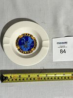 Top view of white ceramic ashtray with NATO SACLANT emblem, showing measuring tape indicating approximately 12 cm diameter.