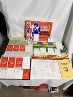 Complete game components laid out on white background including board, player cards, stats sheets, rule sheet, and box.