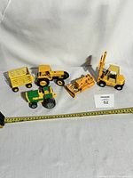 Five vintage metal toy vehicles arranged with measuring tape showing size, on white backdrop.