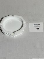White milk glass ashtray with hobnail pattern visible on side, octagonal shape with cigarette rests on rim.