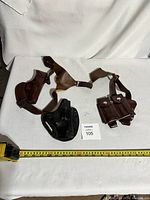 Three RCMP leather holsters arranged on white fabric with measuring tape and lot number card.
