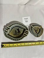 Two Wade Ireland ceramic ashtrays with hunting scene decorations placed on white fabric with measuring tape showing size.