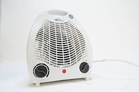 Front angled view of compact white space heater showing front grille and two control dials with power cord trailing.