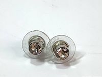 Front view of the Swarovski clear crystal earrings showing the clear crystals set in white rhodium plated metal with clear plastic backings stamped Swarovski.