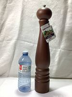 Full view of the Swissmar pepper mill standing next to a water bottle for scale, showing the tall 16-inch height and brown walnut stained wood finish.
