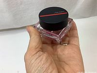 Shiseido blush jar held in hand showing size and branding on black lid with red line.