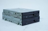 Set of two 3.5 inch floppy disk drives stacked, showing metal sides and black plastic fronts with disk slots and buttons.