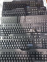 Photo showing stacked pile of 6 Lenovo wired keyboards, black color, USB wired connection cables visible.