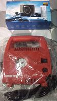 Boxed dash cam and red portable air compressor sealed in plastic with accessories.