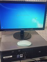 Full view of HP desktop tower under ASUS monitor, white mouse on top of tower, Windows login screen visible