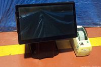 Front view of the POS system, showing the touchscreen monitor and the white Zebra thermal receipt printer positioned beside it on a table.