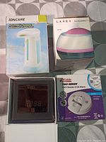 Lot contents showing Ioncare soap dispenser in box, LARES humidifier in box, Kidde smoke & CO alarm in box, and a digital device with display in case.