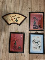 Four antique Asian shadowboxes displayed on wooden surface, showing various floral carvings in black frames