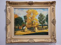 Framed autumn oil painting showing autumn trees in yellow, green, and orange with haystacks and a small white house, in an ornate cream frame.