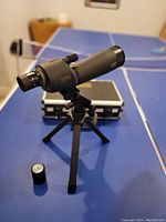 Overall view of the Burris Landmark spotting scope mounted on a tripod with the hard case behind it on a blue table.