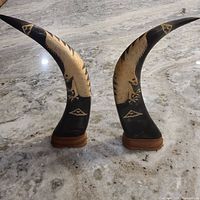 Pair of hand carved water buffalo horns with eagle carvings on a granite surface, showing full height and both sides.
