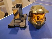 Photo showing Master Chief helmet and black display stand separated on table, front and side visible.