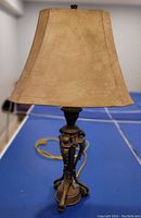 Photo of a bronze table lamp with a beige fabric shade on a blue table.