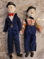 Full view of both Laurel and Hardy dolls showing porcelain heads, hands, fabric bodies, clothing, and shoes.