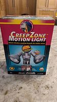 Front view of the boxed CreepZone Motion Light showing branding and product features including dual lights and extra sensor coverage.