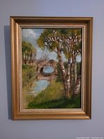 Full view of the framed antique oil painting showing a landscape with a stone bridge, trees, and water.