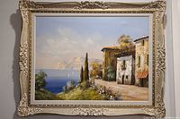 Full view of the framed oil painting showing a scenic Italian shore with buildings, cypress trees, sea and mountains.