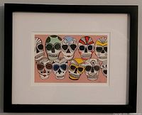 Framed artwork with nine colorful skulls on pink background by Sophia Saunders, showing full piece and frame.