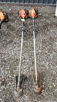 Photo of two long shaft Echo SRM-225 weed-eaters lying side by side on ground, showing overall length and condition
