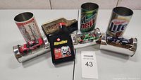 Four NASCAR die cast collectible cars in individual clear display cases presented inside metal promotional cans featuring Budweiser, Havoline, Mountain Dew, and Miller Lite logos