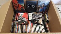 Overhead open box with multiple DVDs inside, highlighting prominent Steelbook cases of Spider-Man 3, Scarface, Terminator, and 2012.