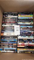 Complete lot of 64 DVD movies arranged in a box, showing a wide variety of titles and cases.