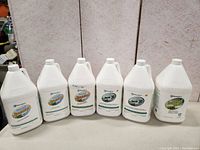 6 white gallon bottles of Beneffect botanical disinfectants and cleaner on a table, showing front labels.