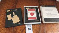 White jumbo oil lighter with red Canadian flag inside a black presentation box with gold text and lighter silhouette image, displayed on wooden surface.
