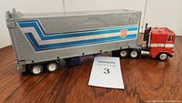 Side view of the red and silver Optimus Prime truck with blue and silver trailer showing Autobot insignia and blue stripes.