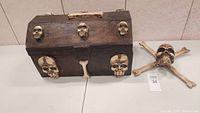 Wooden Halloween trunk decorated with multiple skulls and a crossbones decoration next to it on a table surface