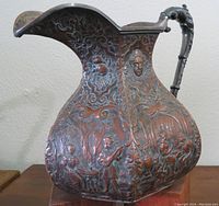 Photo of side of the copper water jug showing musical scene with people and floral details