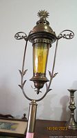 Tall brass processional lantern on a pole with amber glass insert and decorative floral arms