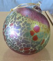 Round multicoloured glass ornament with pink, green, gold cracked pattern, and gold string loop for hanging.