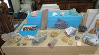 Wide view showing a variety of rock and mineral samples arranged on boxes and a flat surface including raw chunks and polished stones.