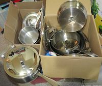 Six stainless steel pots with matching lids arranged in cardboard boxes