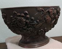 Photo showing side view of metal bowl with raised chrysanthemum flowers and detailed leaves carved in relief around exterior. The bowl has a raised pedestal base and aged patina.