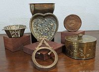 Group of six small decorative metal items including planter, tray, container, frame, medallion, and bowl.
